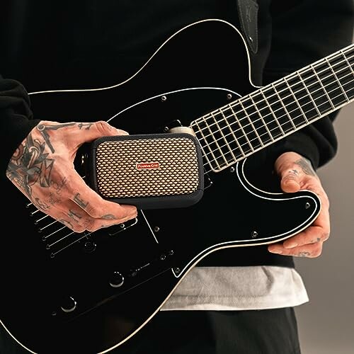 Person holding a portable speaker next to a black electric guitar